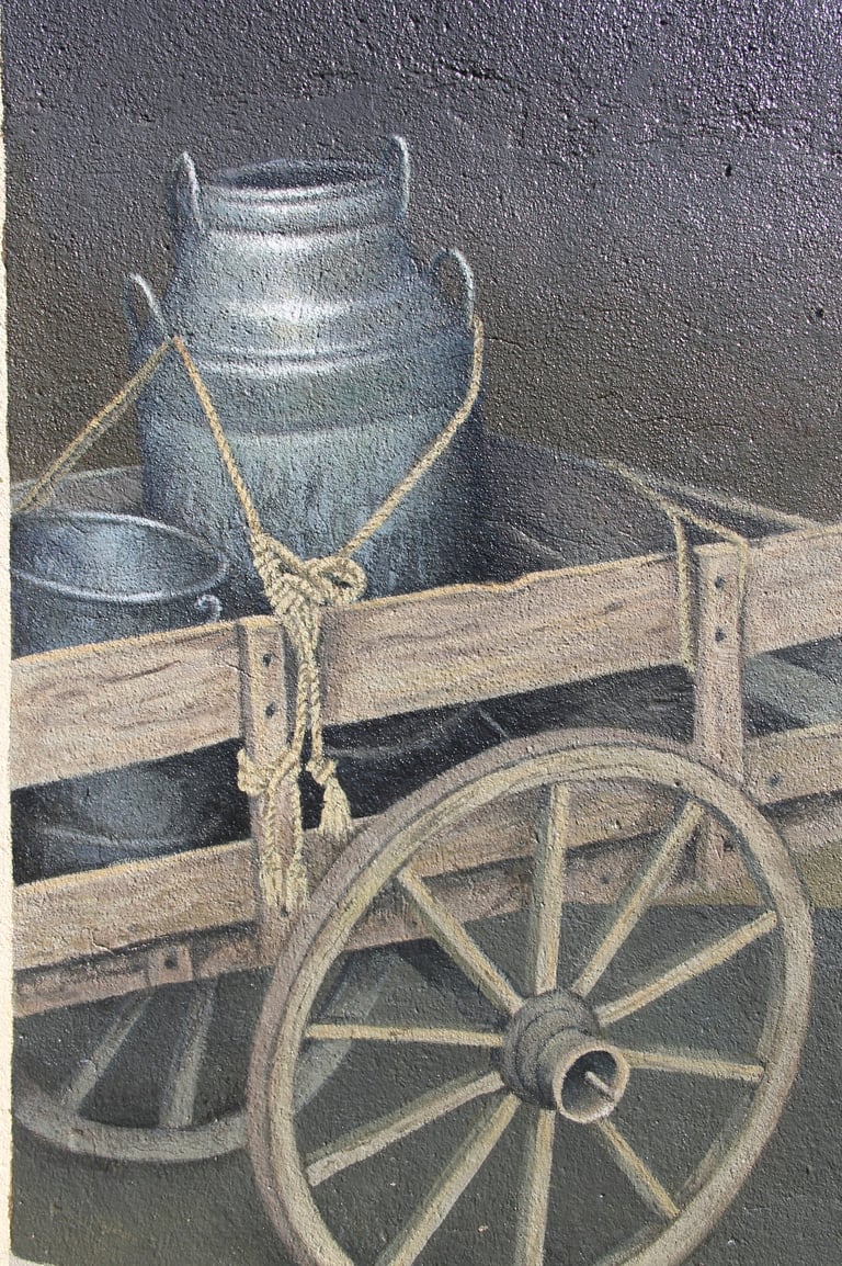 Peinture sur façade d'une charrette en bois avec des bidons à lait anciens tenus par des cordes.