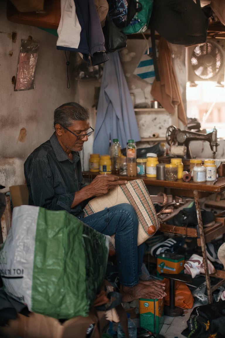 Elderly cobbler hand stitching leather bag in workshop, Mahebourg, Mauritius