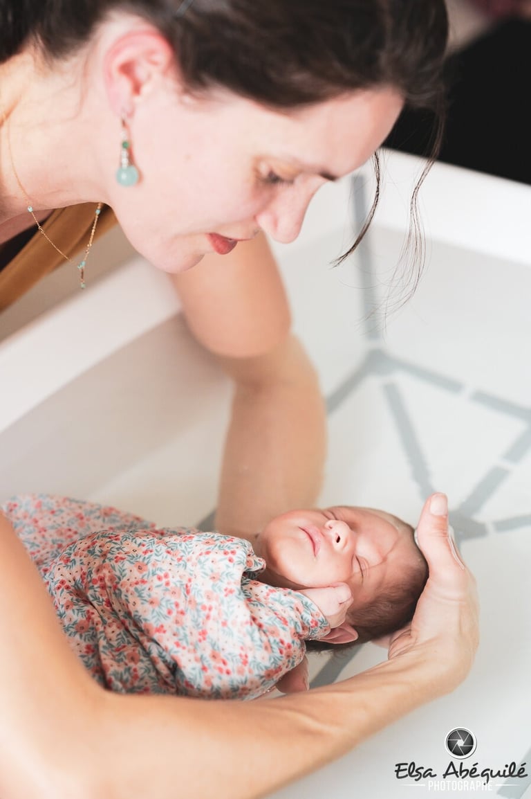 Bébé emmaillotté dans une couverture, dans les bras d'Audrey pendant le Bain des Merveilles