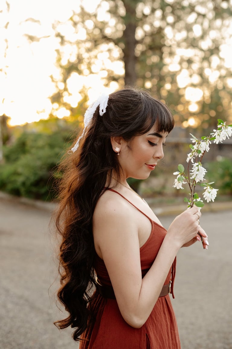 Side profile of Ryanne with long hair and a hairbow holding branch of blossoms in golden hour light.
