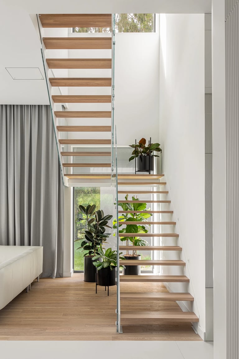 Nowoczesna klatka schodowa, drewniane stopnie, szklana balustrada i duże rośliny w donicach.