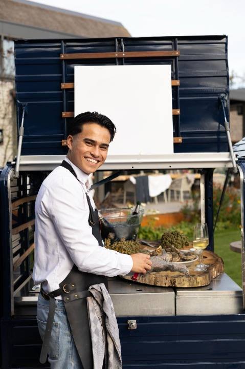 Vrolijk lachende medewerker opent oesters voor de Xagis tuc-tuc foodtruck.