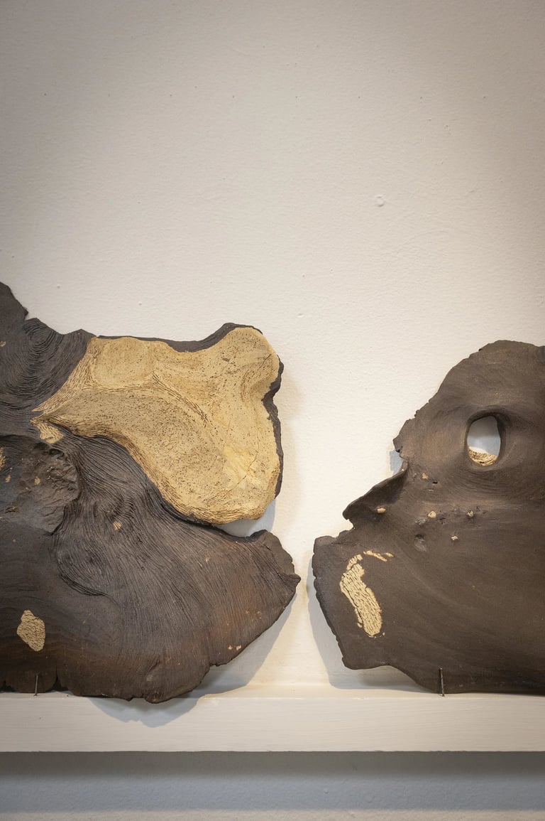 Two abstract hand-formed ceramic sculptures with organic textures and gold leaf accents on a white wall.