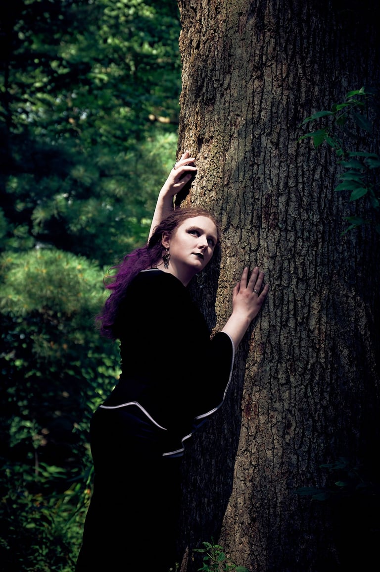 a woman with purple hair in a black dress in the forest with sunlight on her face