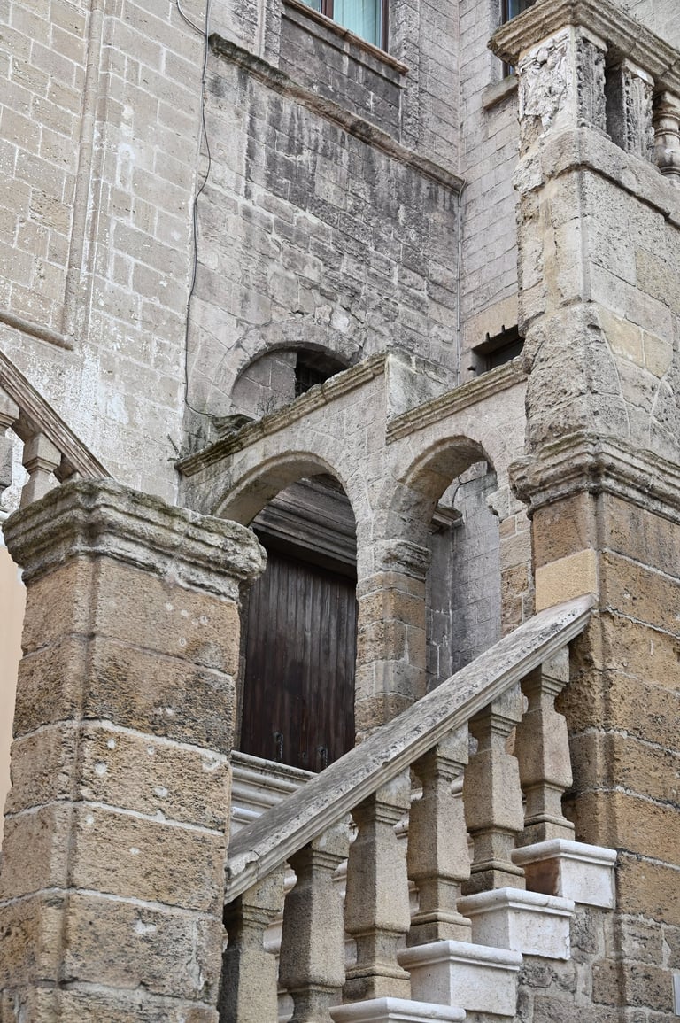 Historic stone staircase with arched balustrade and weathered limestone facade of an ancient building.