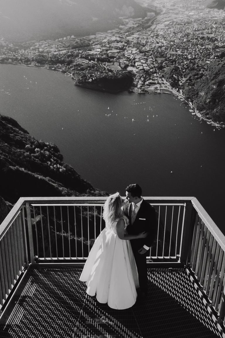 a bride and groom standing on a balcony railing overlooking a mountain
