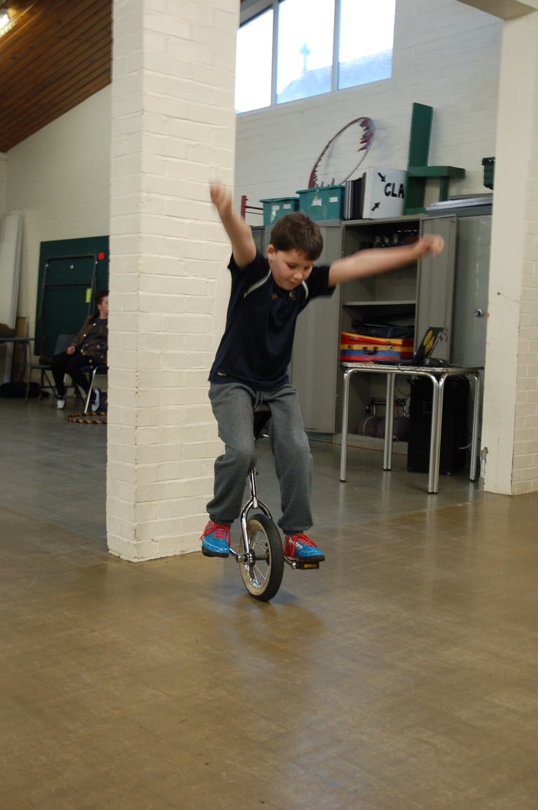 A young boy balances with his arms out while riding a unicycle .