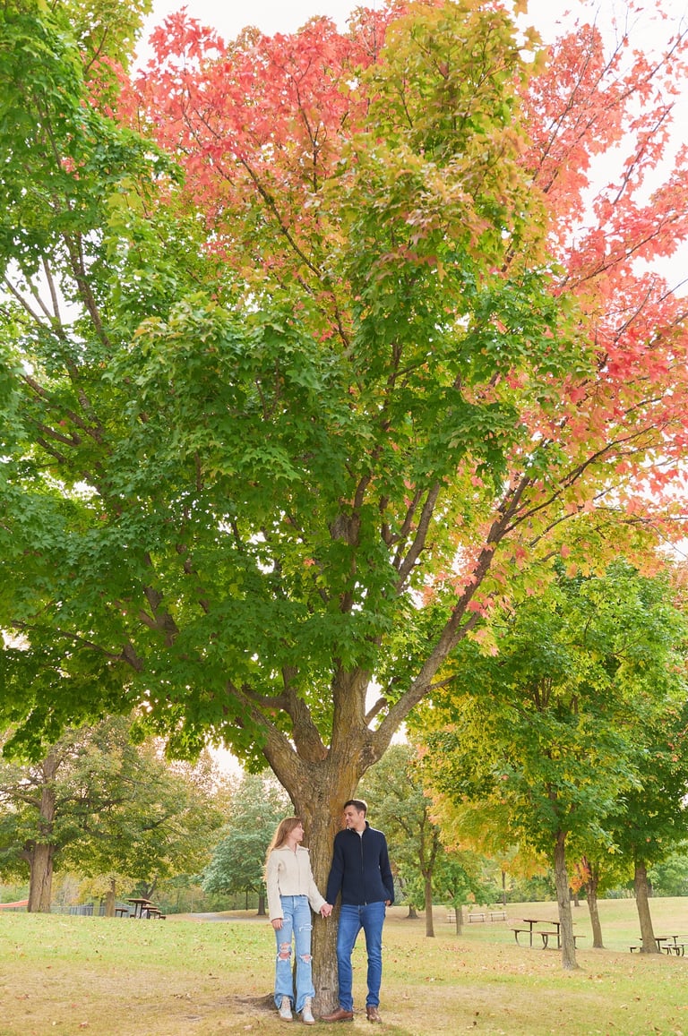 a man and woman standing in front of a tree with red leafs looking at each other