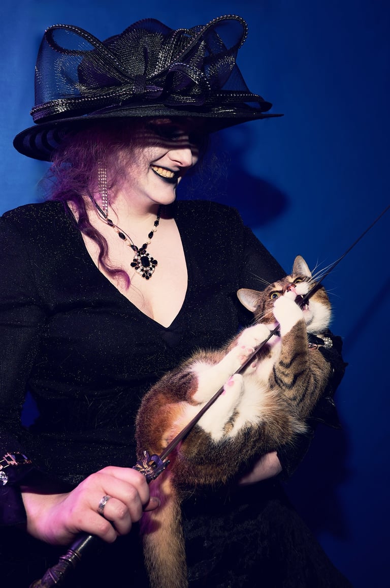 a woman in a black hat holding a cat which is biting a sword