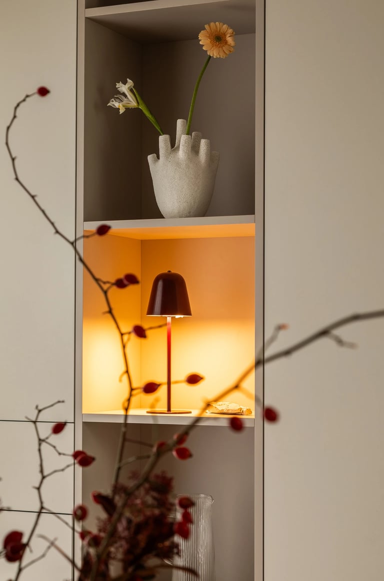 Detal regału: wazon w kształcie dłoni, lampka i książki na półce.