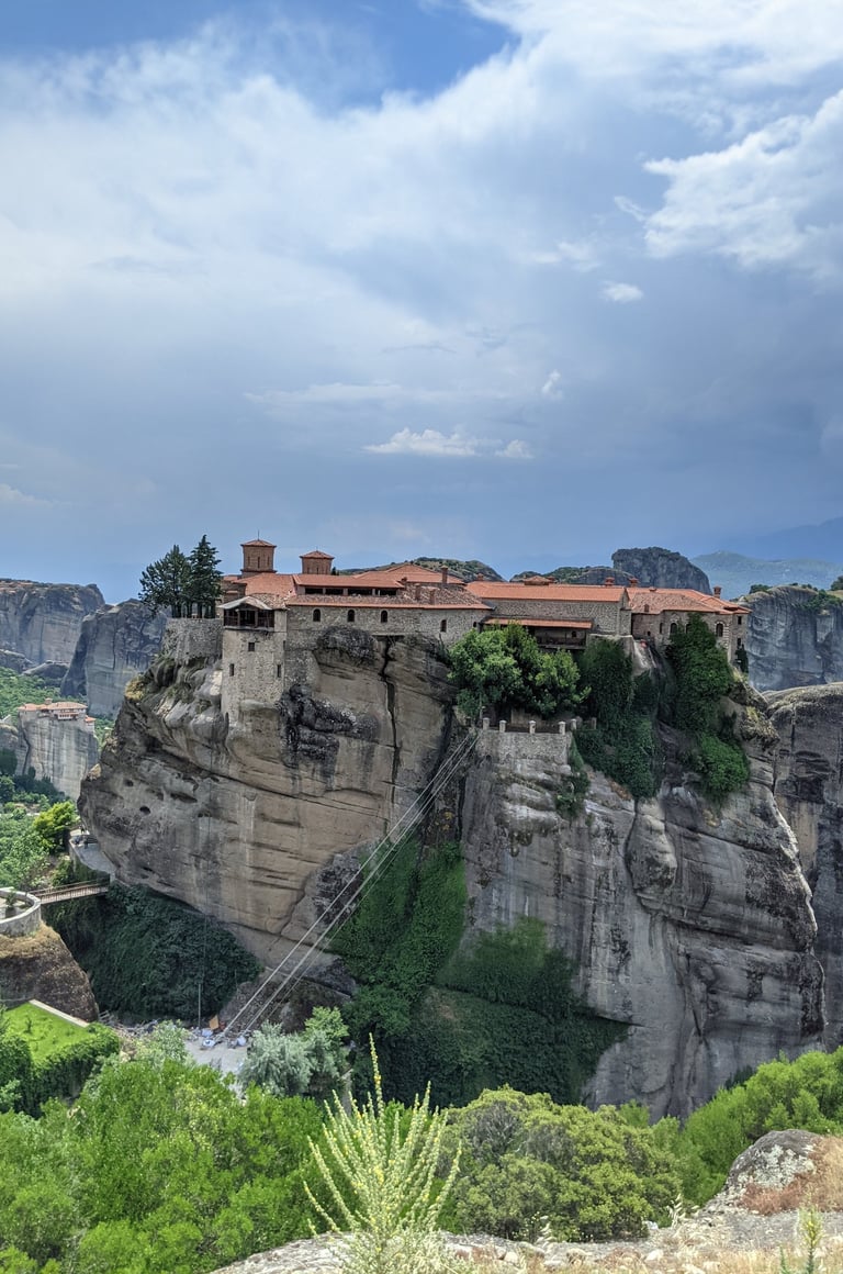 A red roofed monastery in Meteora, Greece perched precariously on a rock spire. 