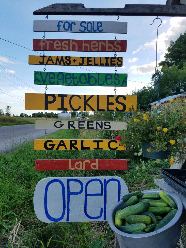 A farm stand with hand painted sign that says for sale: fresh herbs, jams and jellies, vegetables,