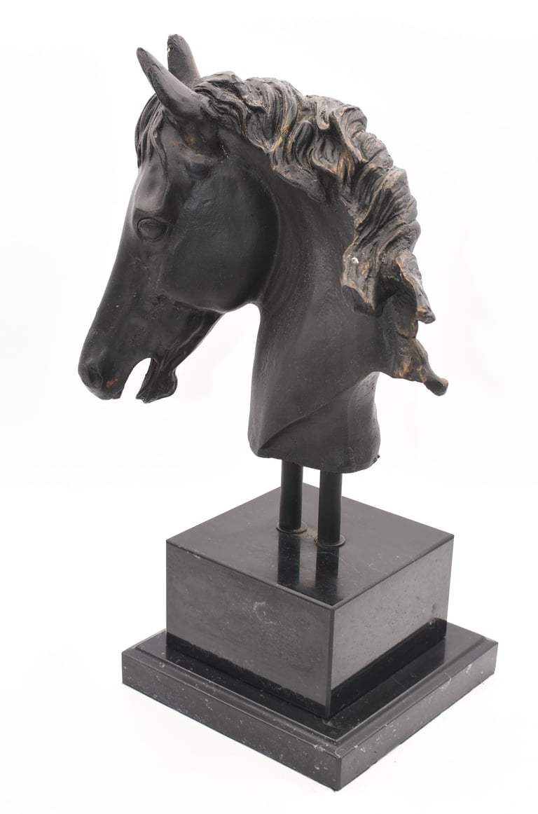 A dark bronze color horse head sculpture with a flowing mane mounted on a tiered black pedestal.