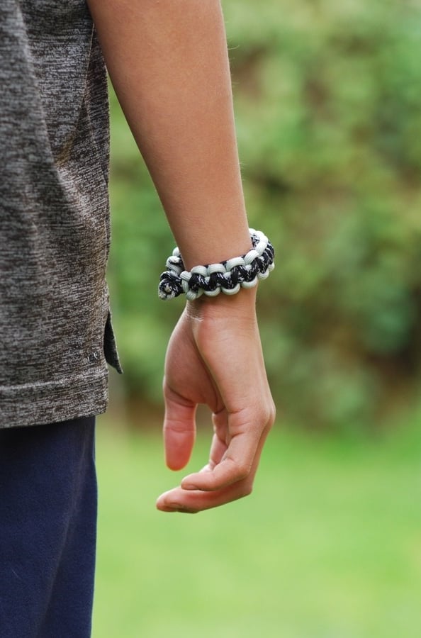 a paracord bracelet on a person's wrist with a green nature background