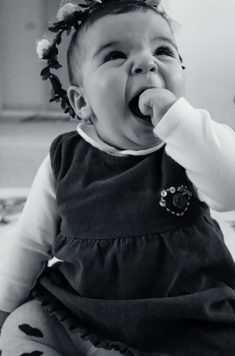Black and white portrait of a happy baby girl wearing a floral headband and corduroy dress.