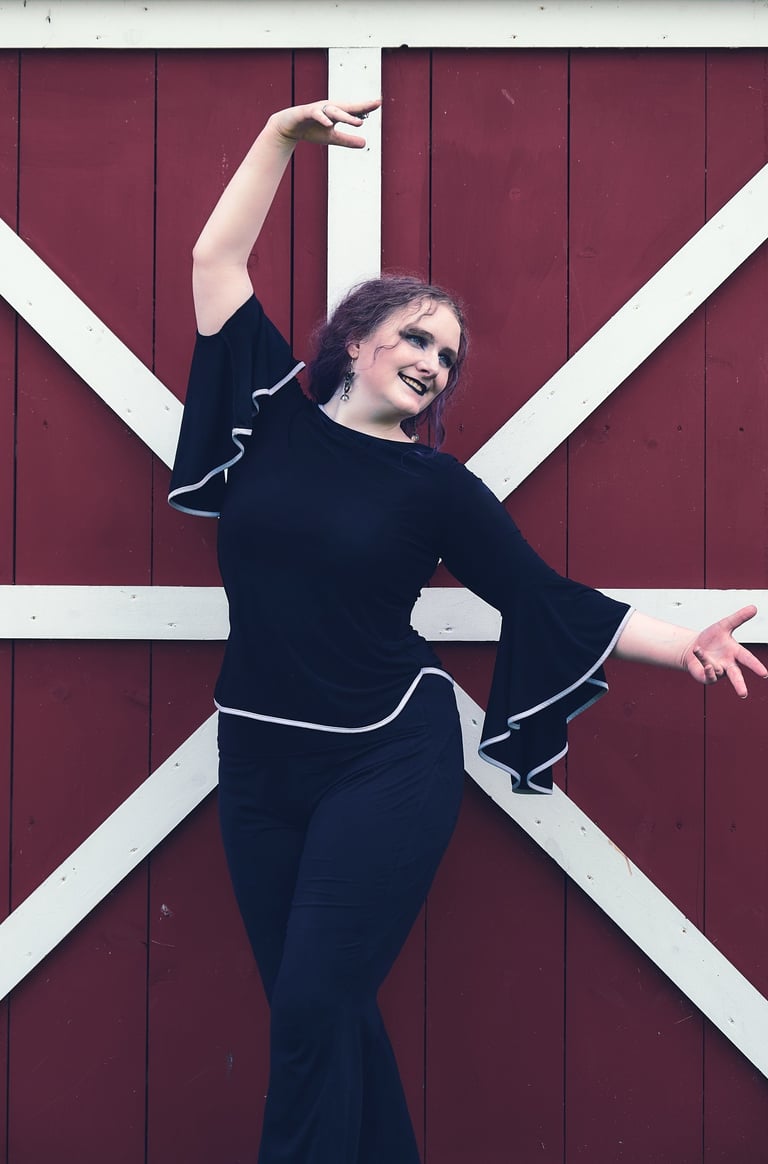 a woman in a black top and pants dancing in front of a barn
