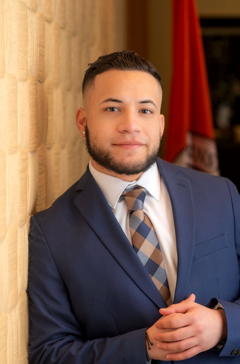 Isaac Vasquez in a blue suit with a white undershirt and blue and brown tie.