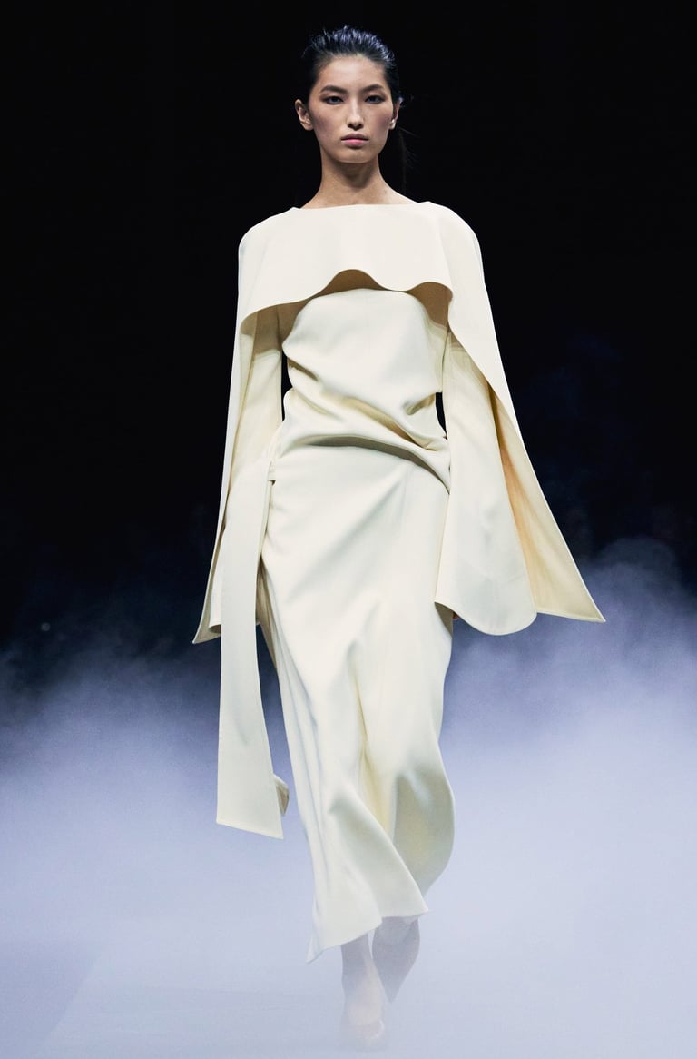Khaite Spring/Summer 2026 runway model in an ivory long-sleeve gown with cape detail.