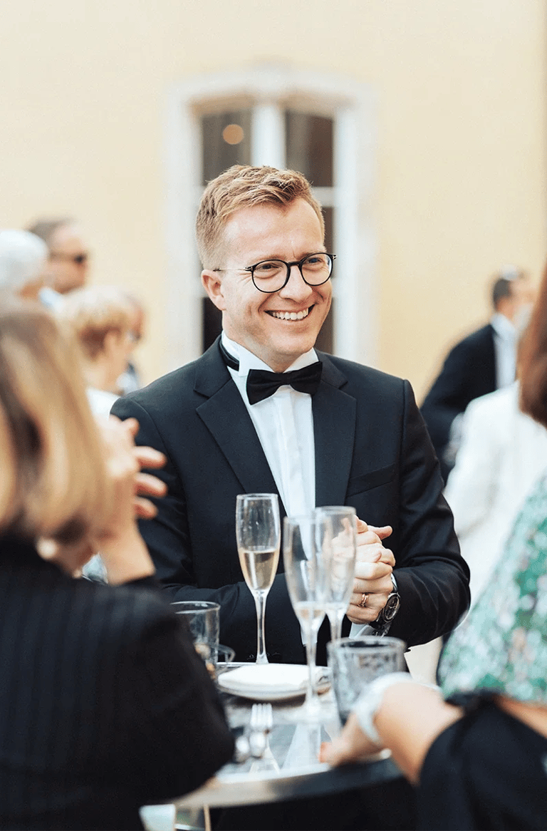 Marié élégant en costume souriant et discutant durant le vin d'honneur.