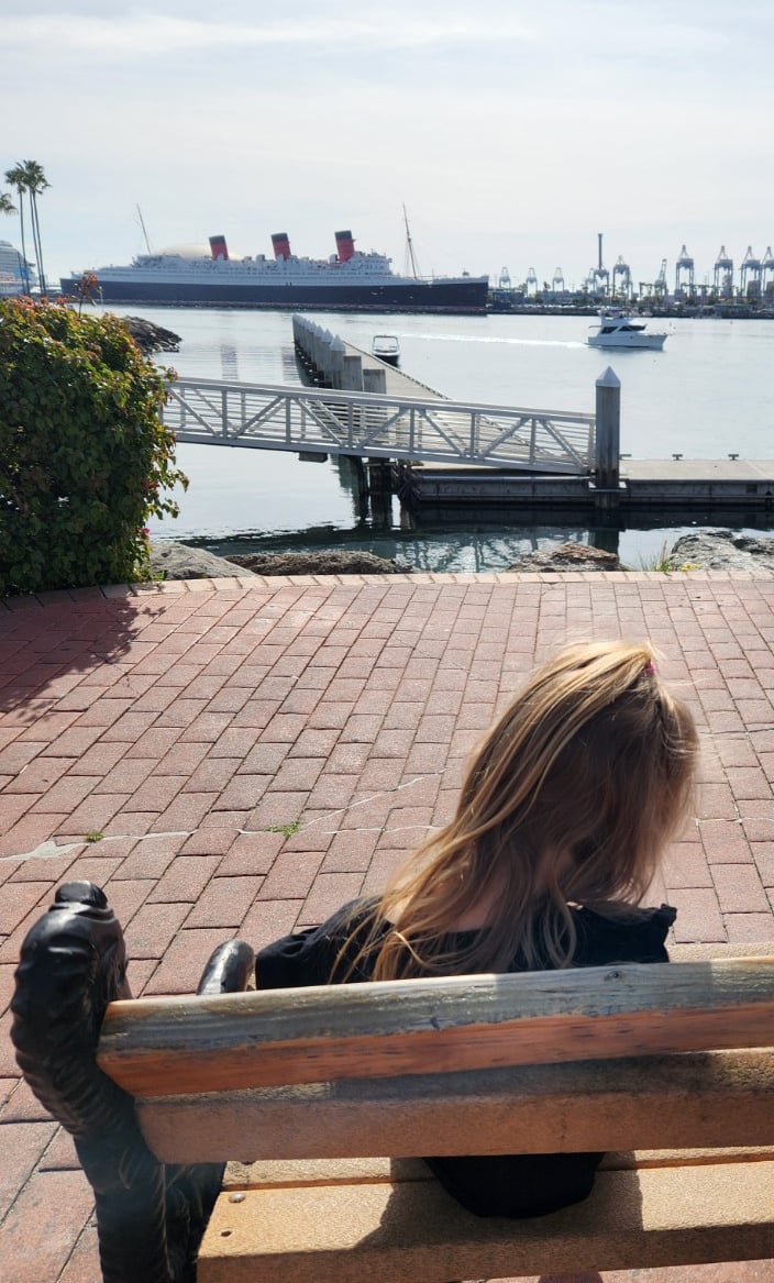 Child sitting on a waterfront bench at Shoreline Village in Long Beach with views of the Queen Mary