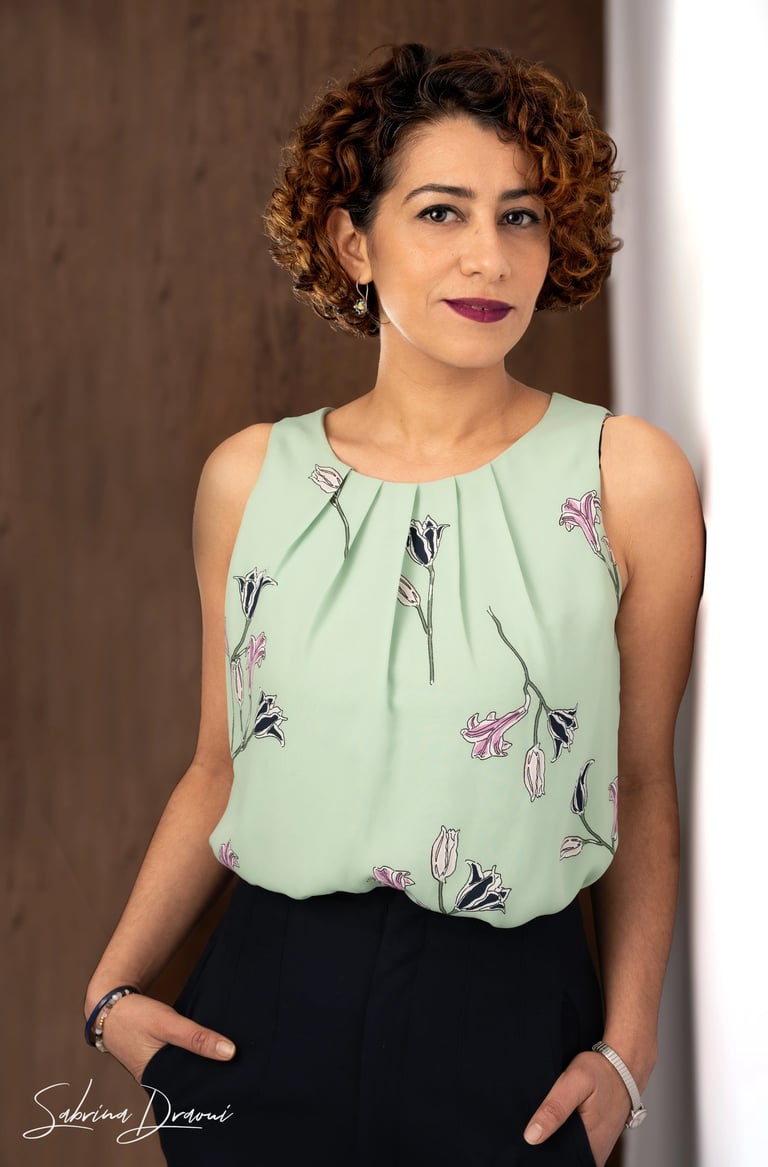 a woman in a green blouse and black pants leaning against a wall