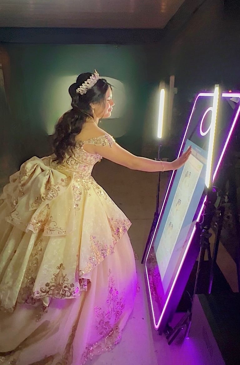 Elegant quinceañera interacting with illuminated mirror booth in a sparkling blush and gold gown.