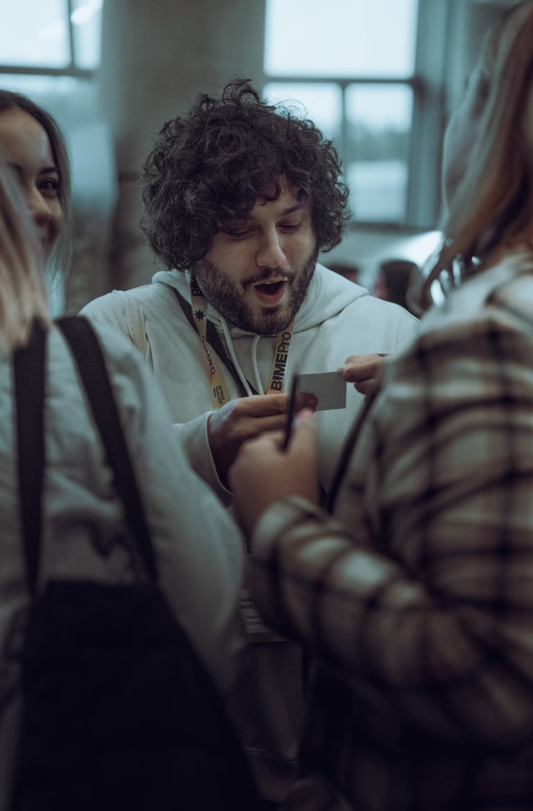 Man with curly hair wearing a BIME Pro lanyard exchanging business cards with two other attendees at BIME Bilbao. Networking 