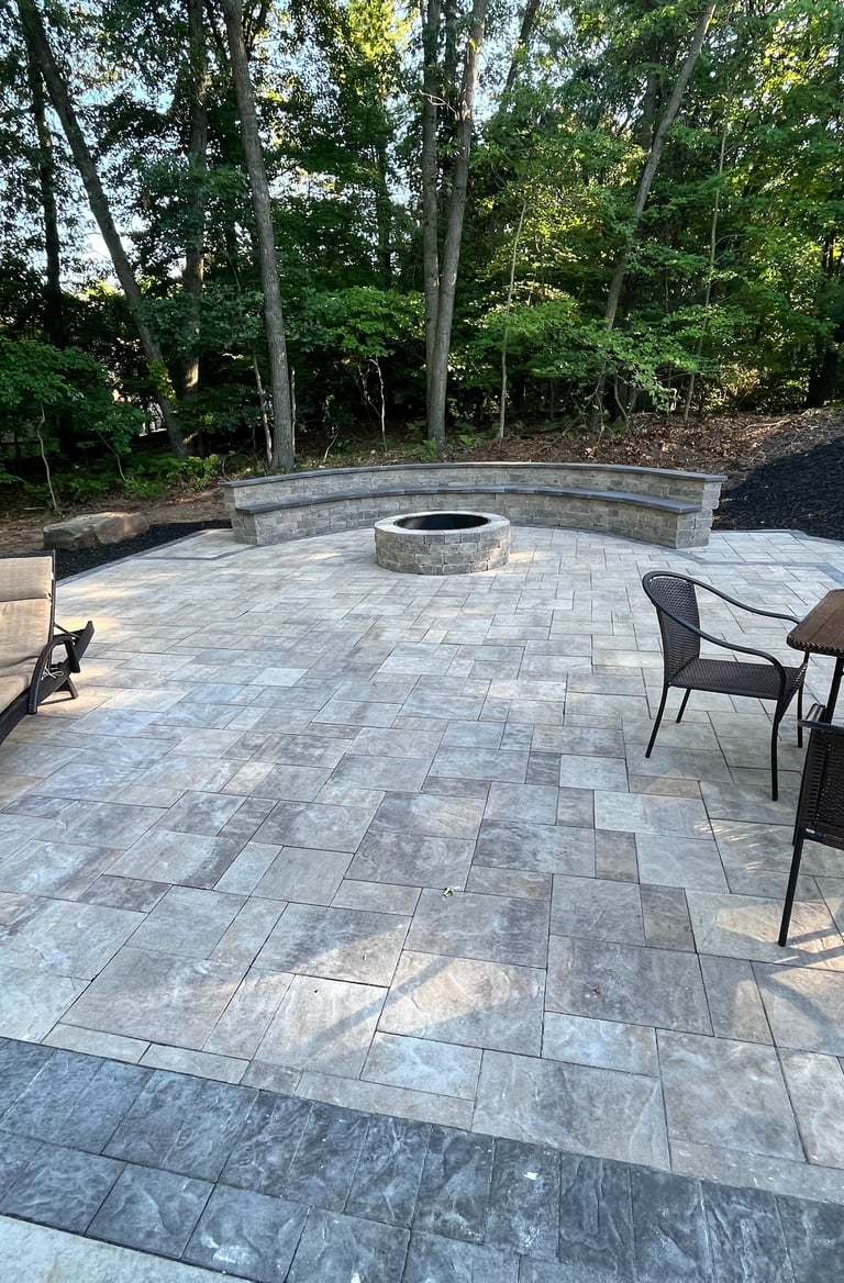 Custom stone paver patio featuring a round fire pit, curved stone bench, and outdoor dining furniture.