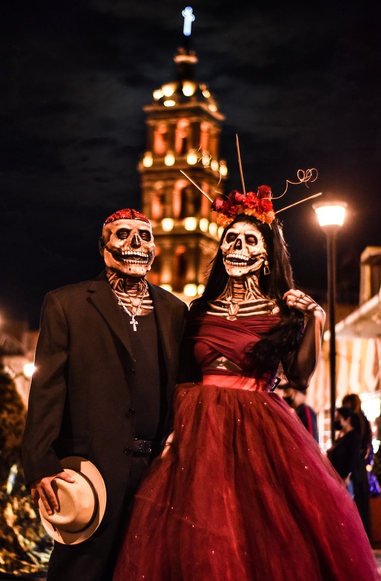 Couple in skull masks celebrating Day of the Dead in front of a Mexican cathedral.