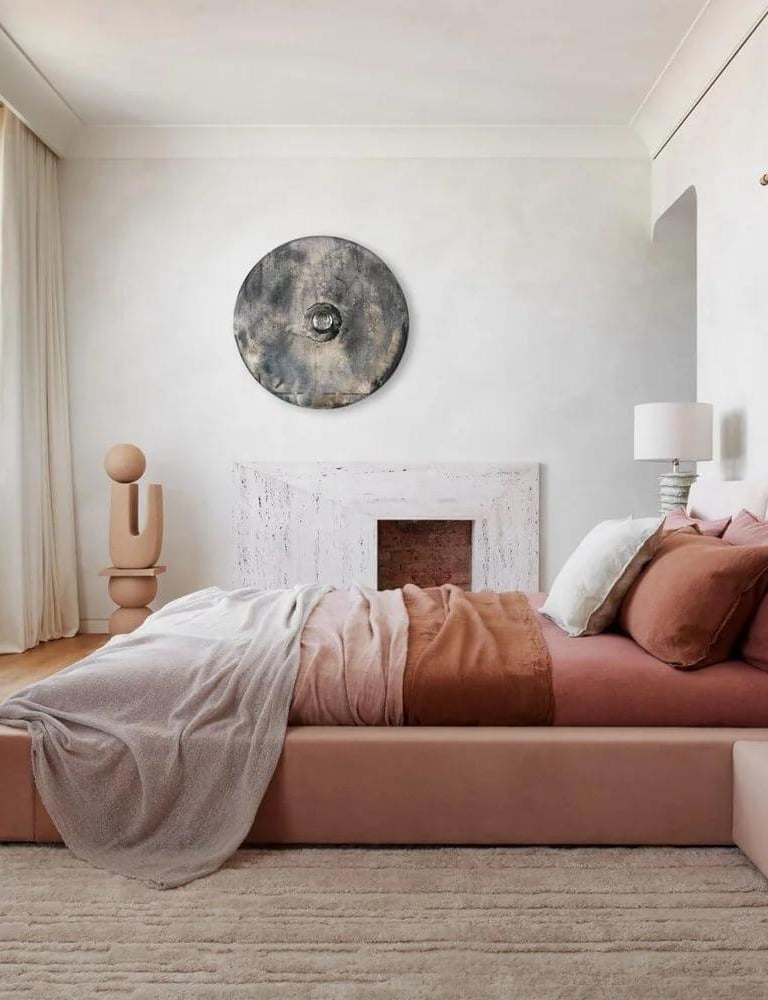 Cozy pink bedroom with layered pillows, warm bedside lighting, and neutral wall decor