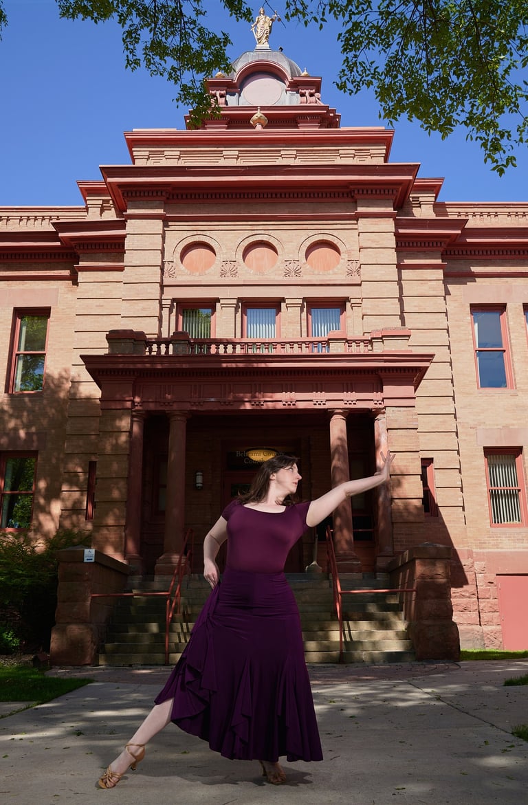 a woman in a purple dress is dancing in front of a historical building