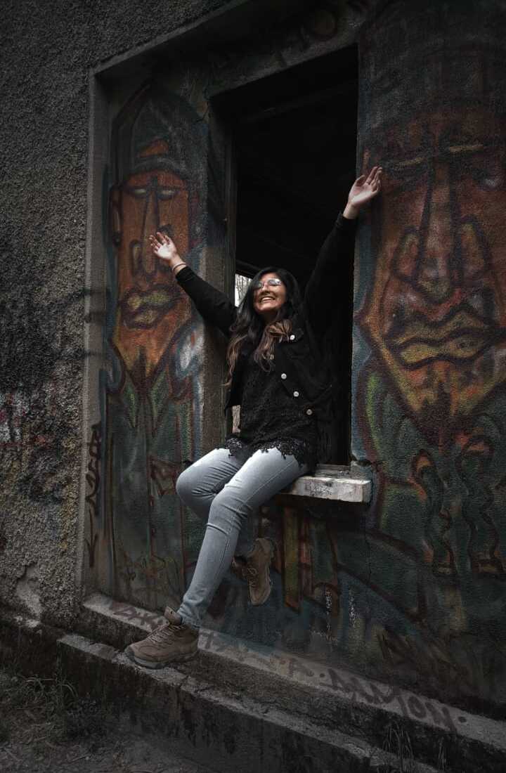 Una mujer sonriente sentada en la ventana de un edificio abandonado, rodeada de arte de grafiti