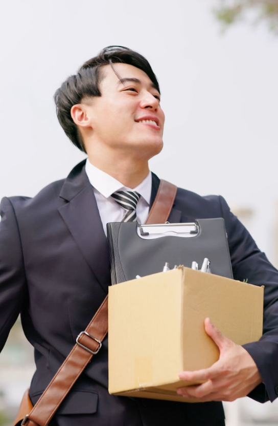 Homme souriant en costume portant un colis et un classeur.