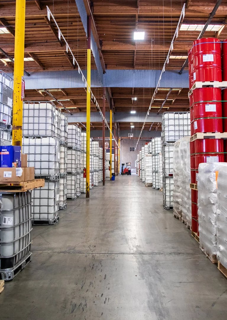 Warehouse with barrels stacked on pallets containing chemicals, acids, solvents, and caustic lye