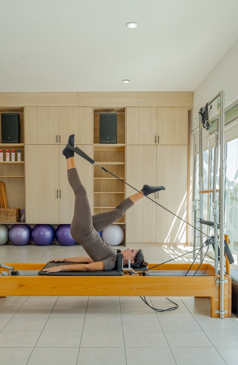 Woman lying on a Pilates Reformer doing a leg exercise using the foot straps in the Cabo San Lucas studio.