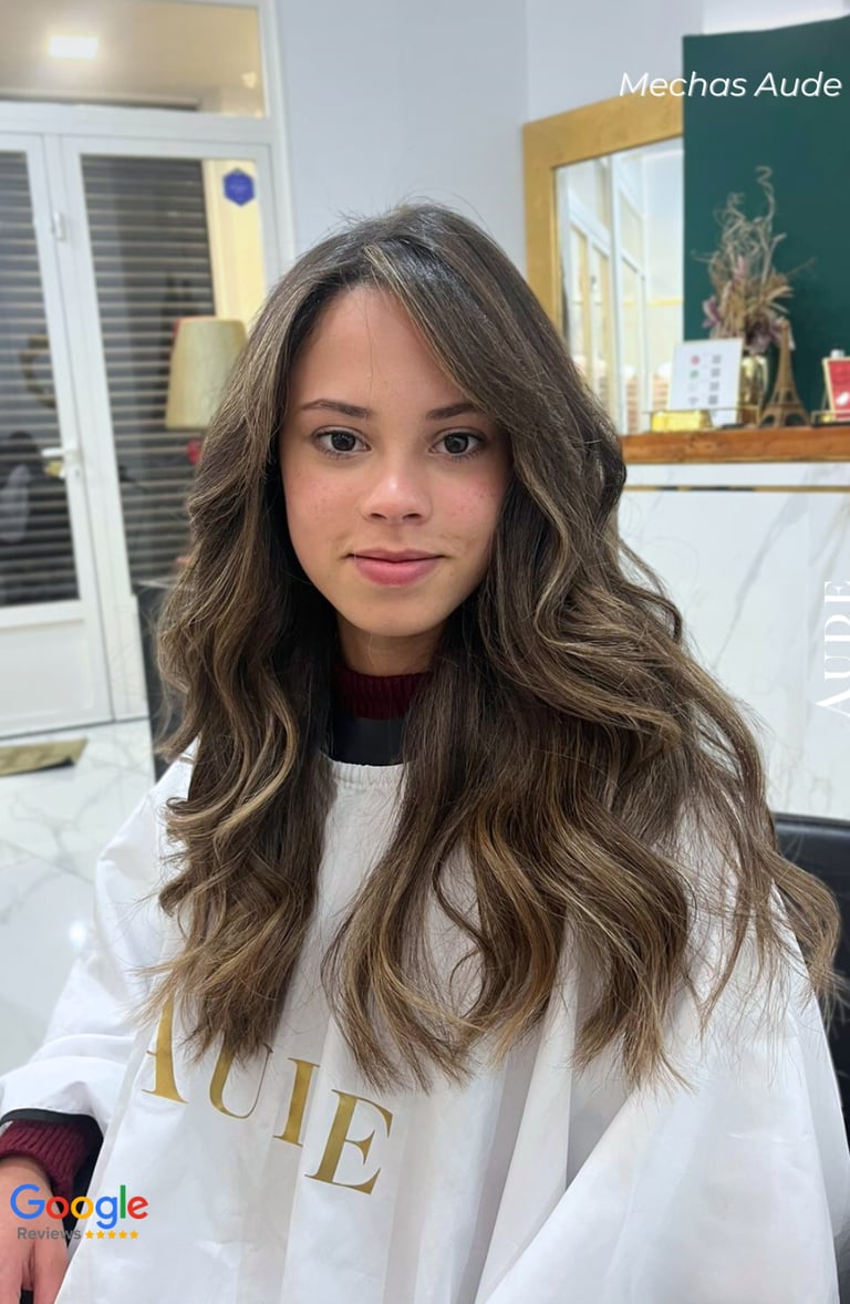 Young woman with long, wavy brown hair and blonde balayage highlights styled at a professional salon.