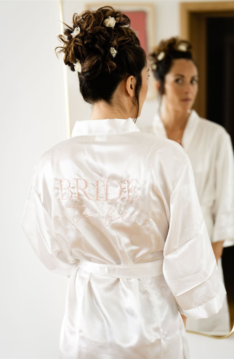Bride in robe marked 'Bride' looking in mirror — fine art wedding preparation in South of France