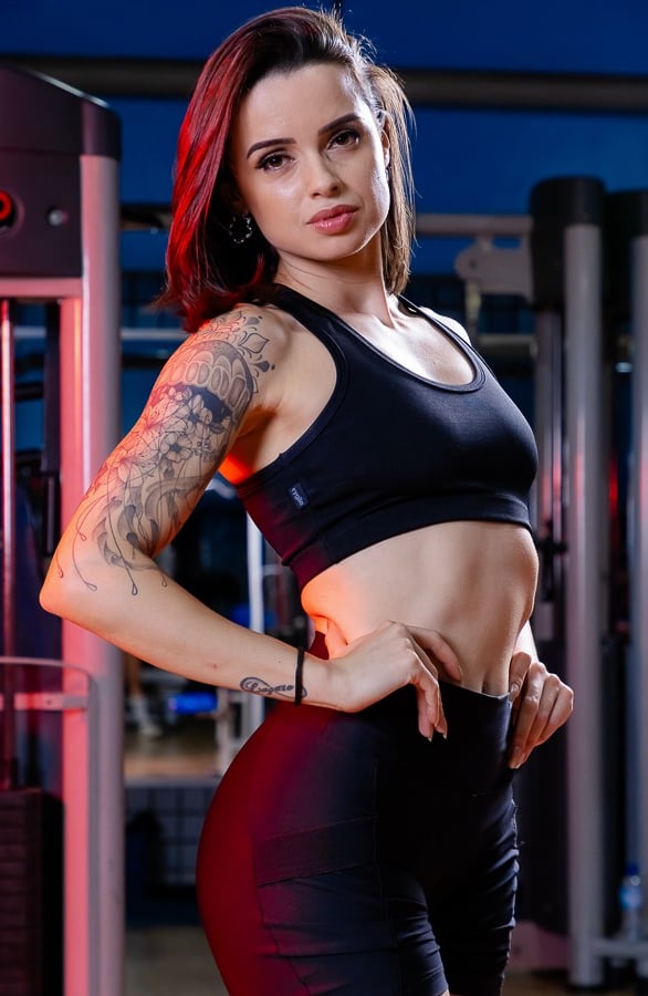 mulher na academia com mãos na cintura fundo colorido