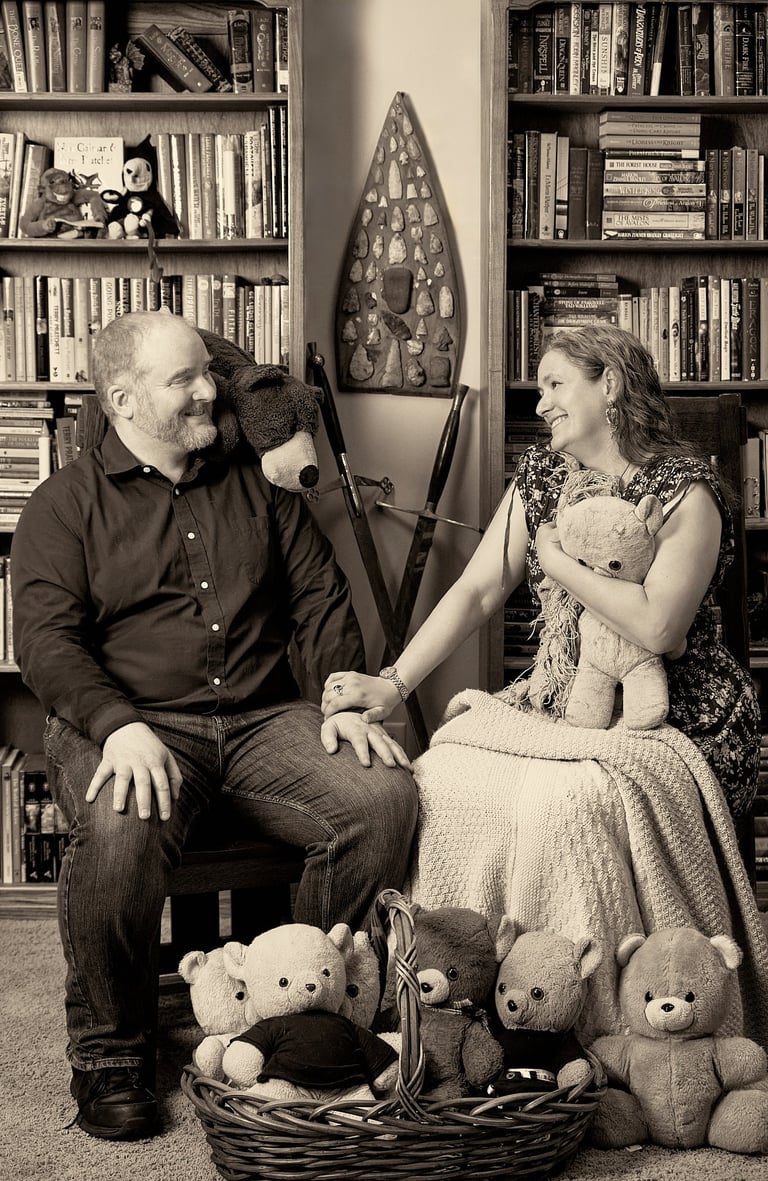 a man and a woman sitting on a chair holding a teddy bear in a library room