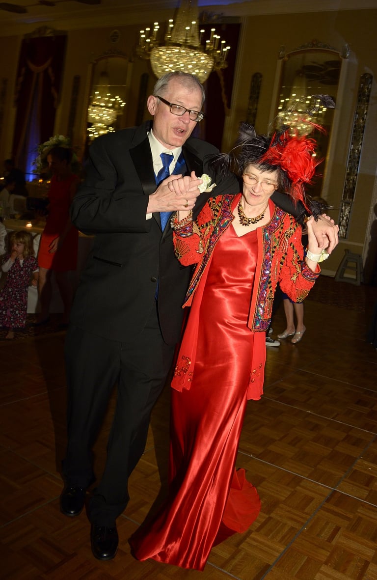 a man in a black suit and blue tie and a woman in a red dress dancing at a dance floor in a wedding