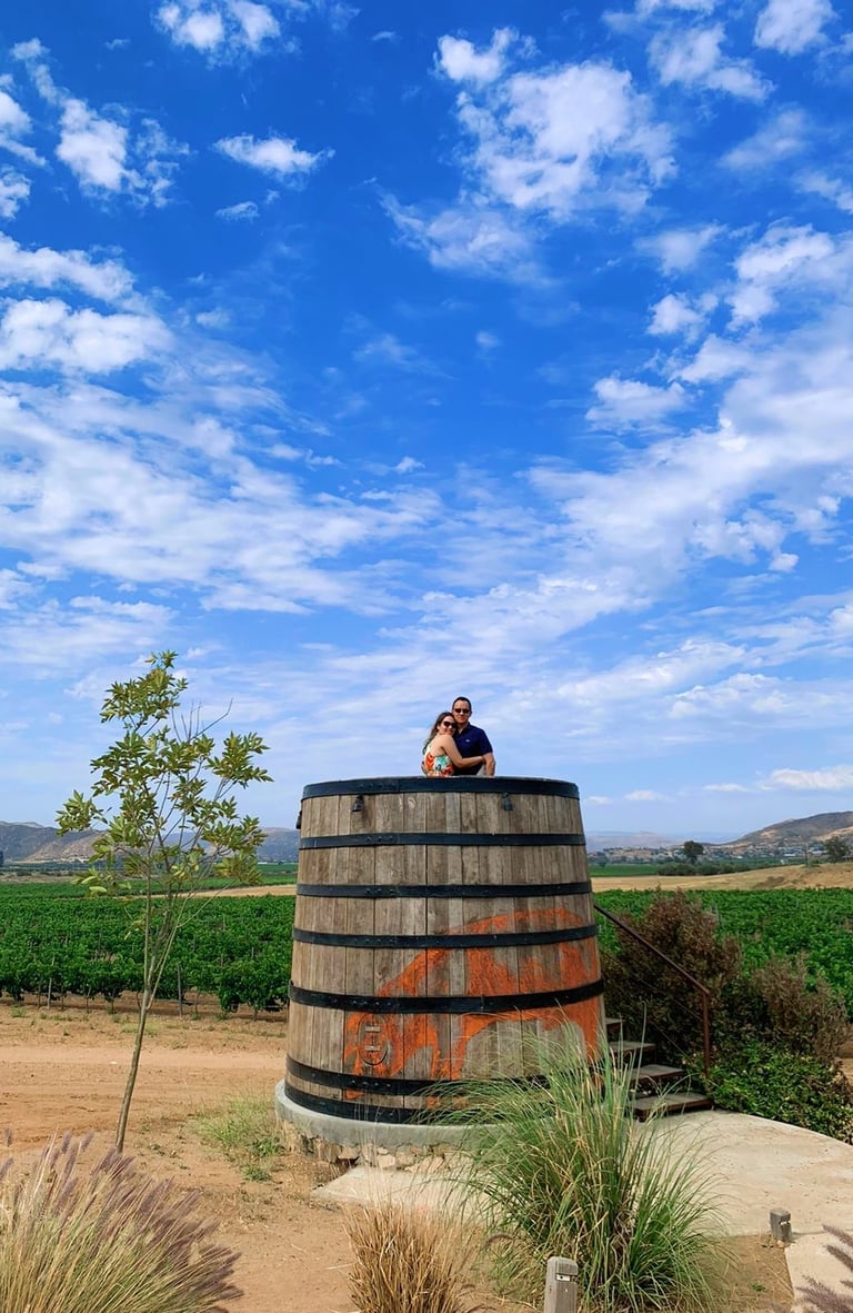 a couple sitting on a barrel of wine enjoying the view of the vineyards of Valle de Guadalupe