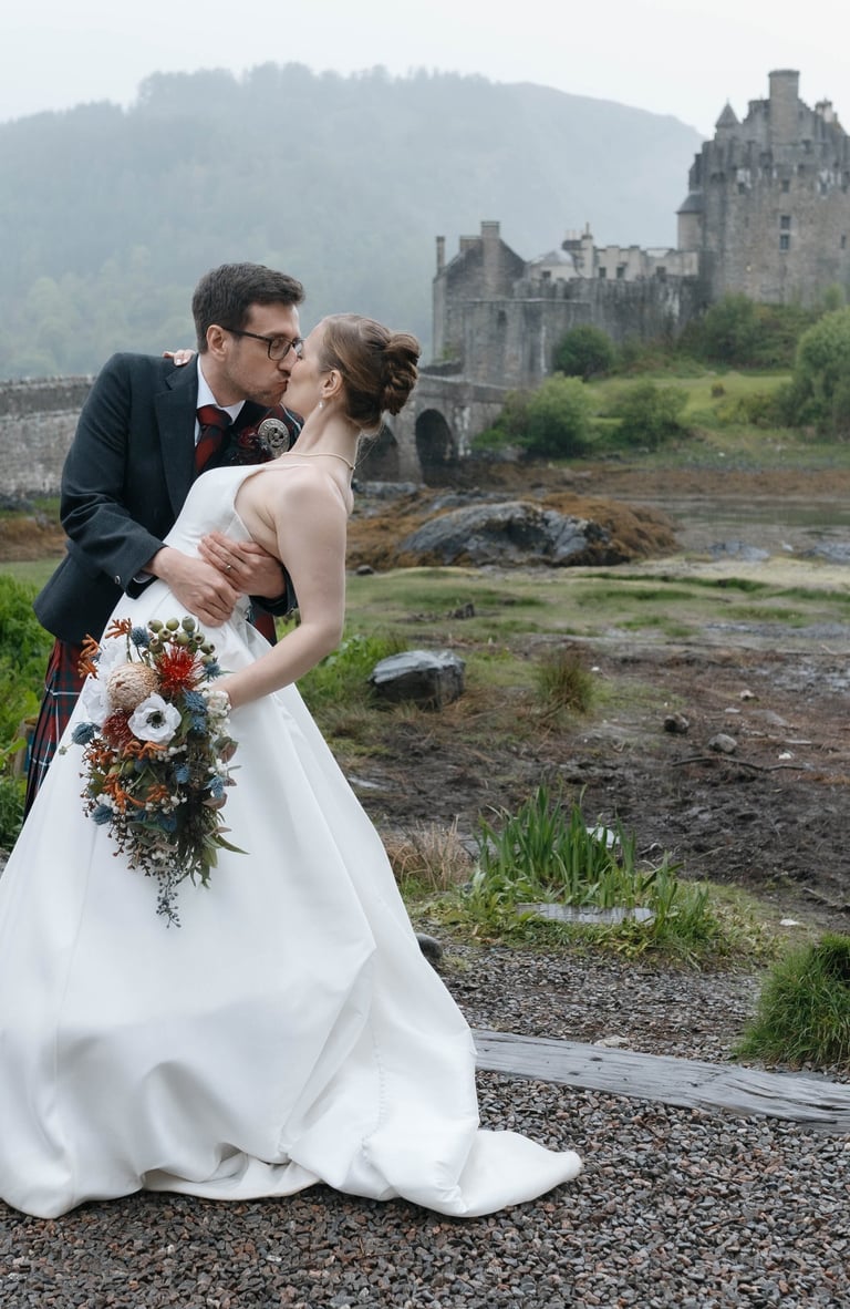 A bride and groom kissing during an elopement at Eilean Donan Castle in the Scottish Highlands.