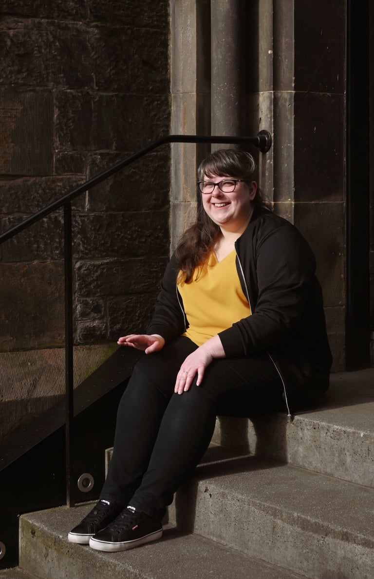 Laura is sitting on stone steps looking just off camera smiling at the sunshine