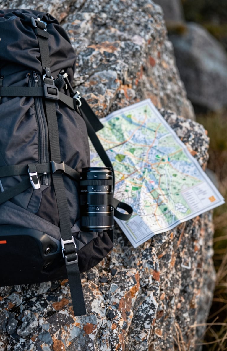 Close-up of adventure gear and a map on a rocky ledge. The aesthetic is rugged yet elegant, focused on real-world storytelling.
