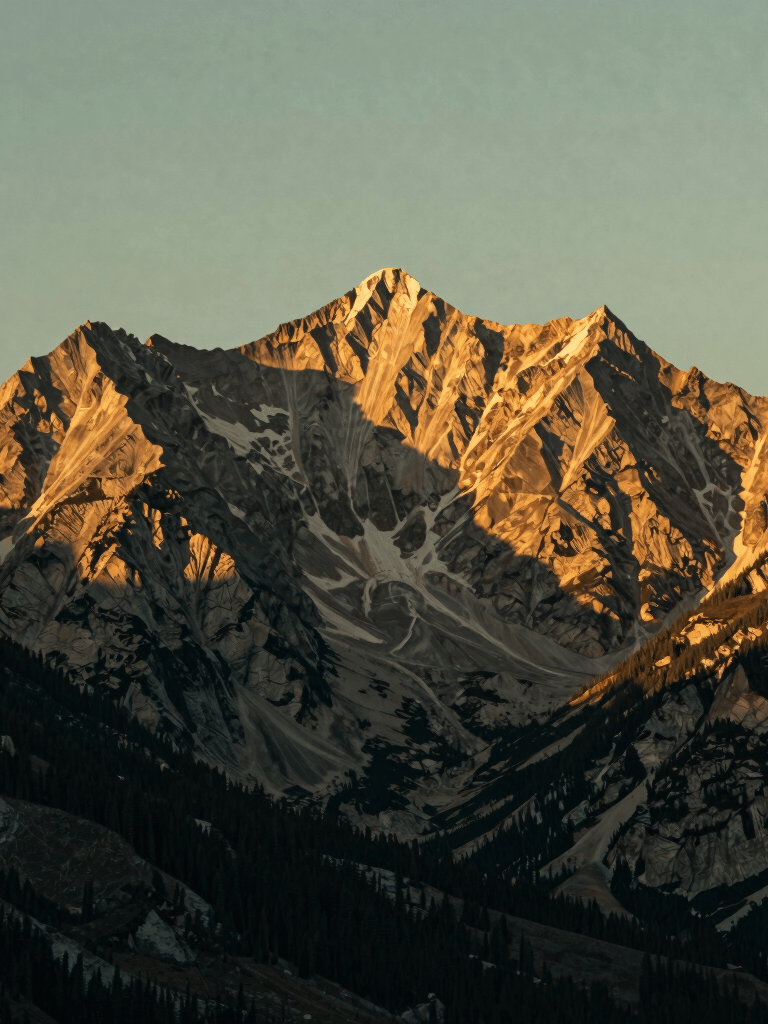 Golden hour sunlight hitting the rugged peaks of a North American / US mountain range, muted gold and sage green tones, cinematic lighting, serene landscape photography.