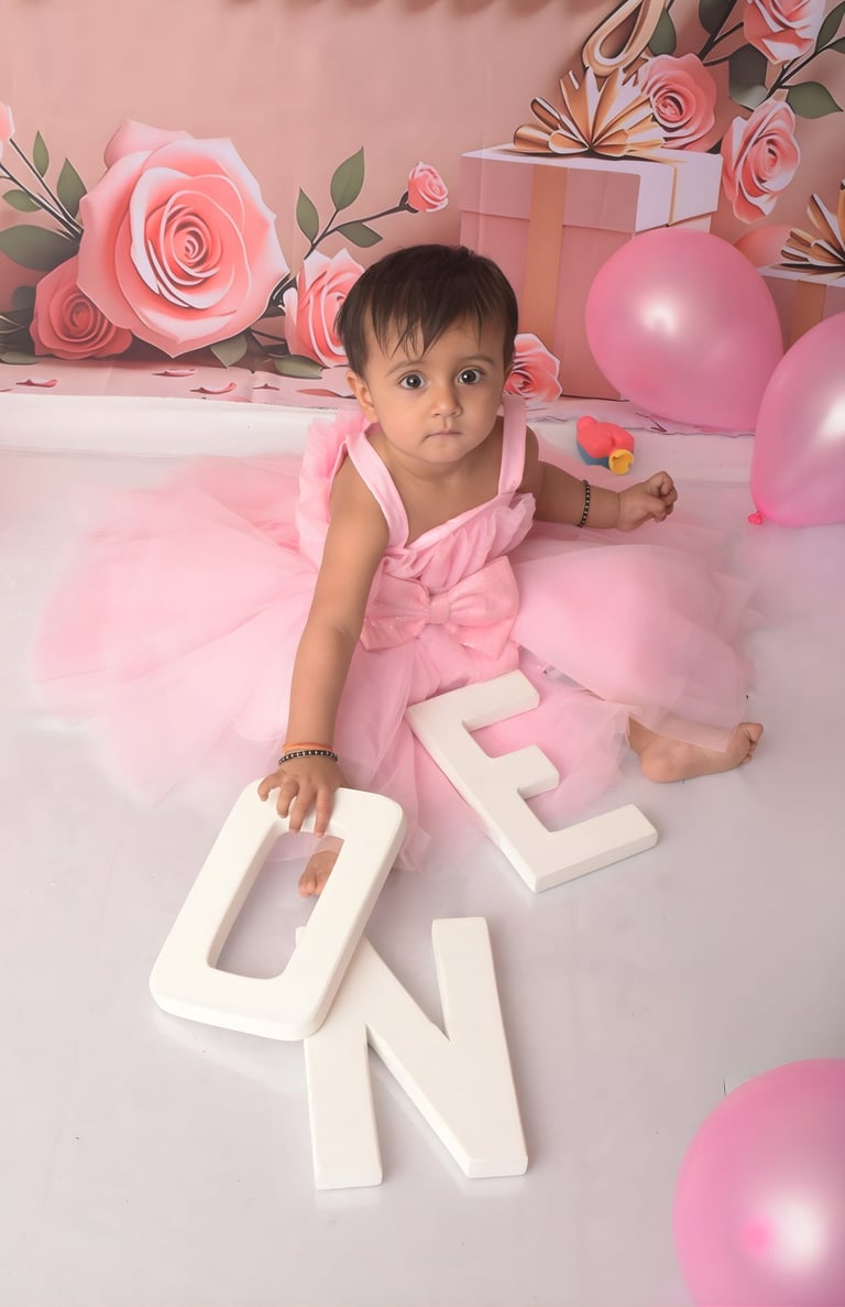 Baby girl in a pink tutu dress celebrating her first birthday with ONE letters and balloons.