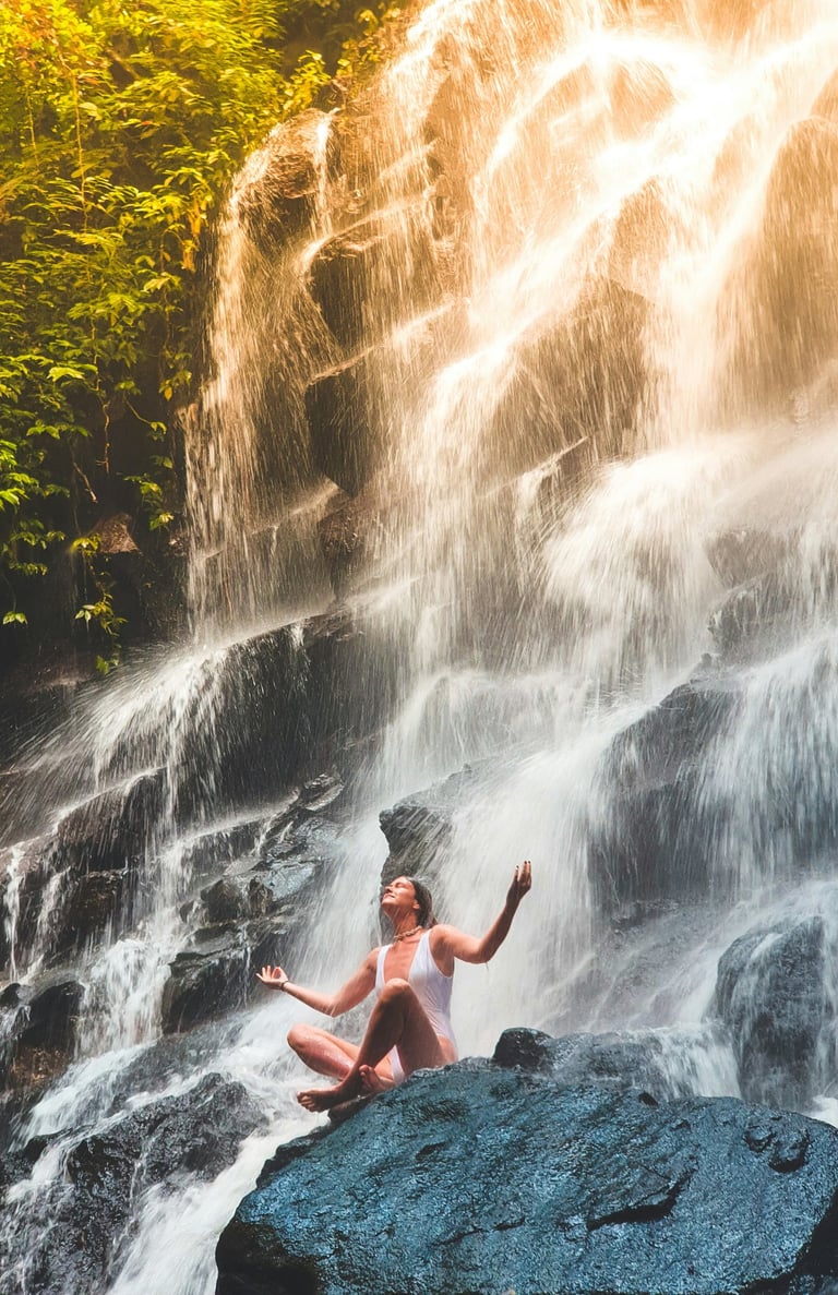 a woman embracing nature while sitting on a rock in front of a waterfall