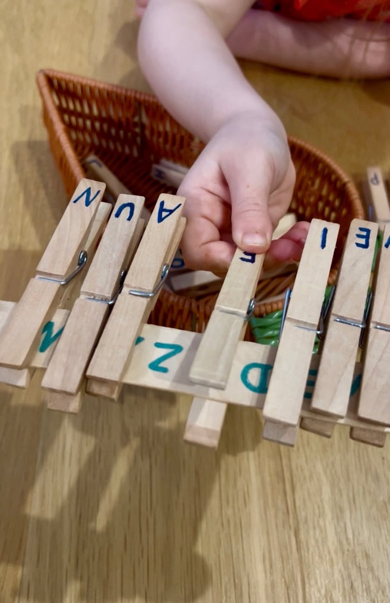 A child practices fine motor skills using wooden clothespins with letters for a DIY alphabet matching activity.