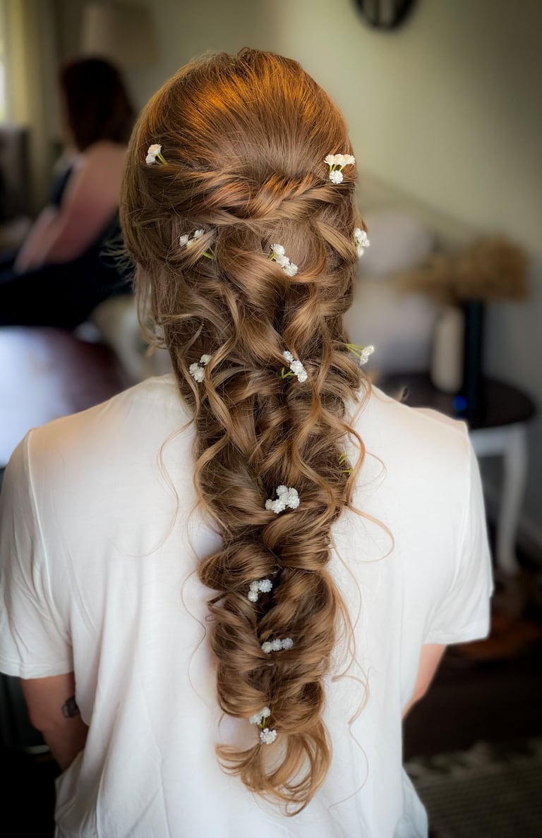 Brunette bride with long boho braid adorned with delicate white flowers, styled in loose romantic curls for wedding day hair.