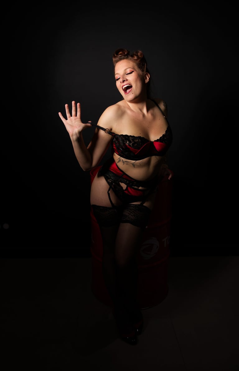 Glamour. Femme en lingerie rouge et noire qui se déshabille en souriant.